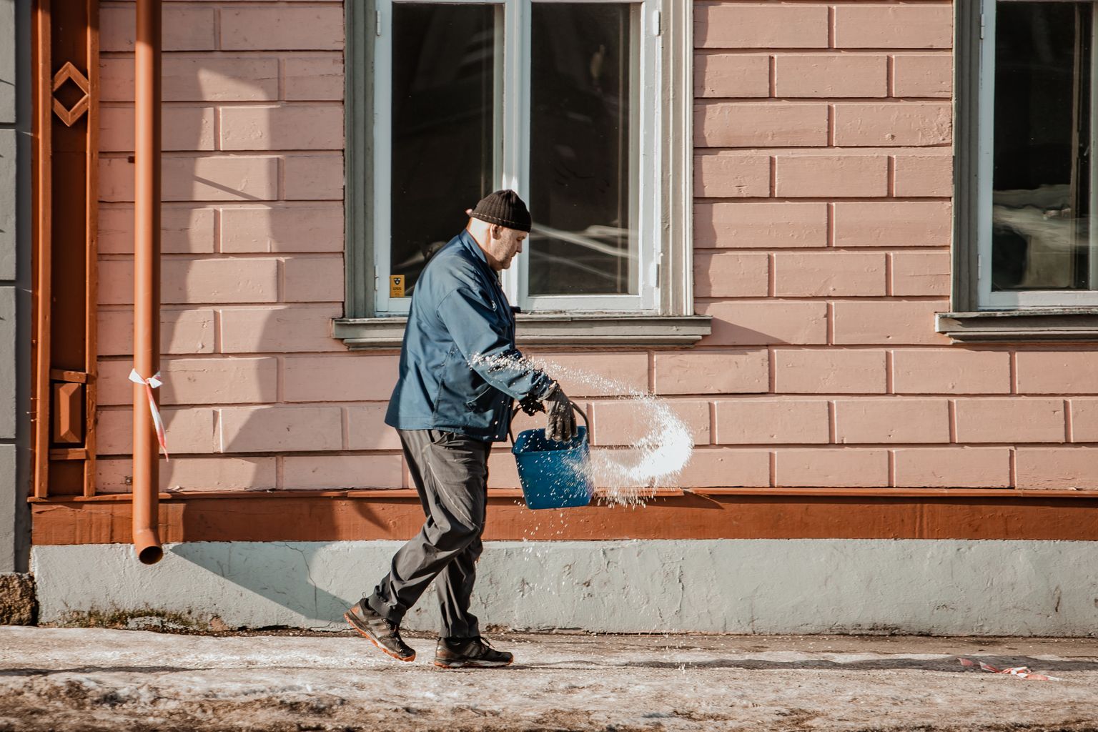 Mees puistab soola libedale kergliiklusteele.