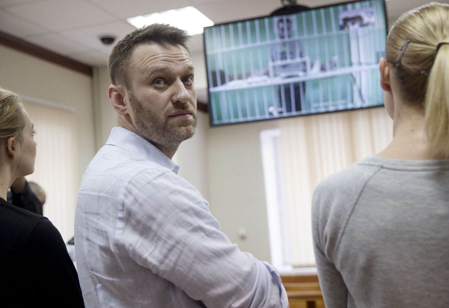 Russian opposition activist and anti-corruption crusader Alexei Navalny, center, his wife Yulia, left, and his brother Oleg's wife Victoria attend a video call with Oleg, shown on a TV screen, at a court in Moscow, Russia, Tuesday, Feb. 17, 2015. Oleg Navalny was convicted on Dec. 30, 2014 and sentenced for three and a half years. Alexei Navalny was also convicted and sentenced to the same prison term, but it was suspended. (AP Photo/Pavel Golovkin)