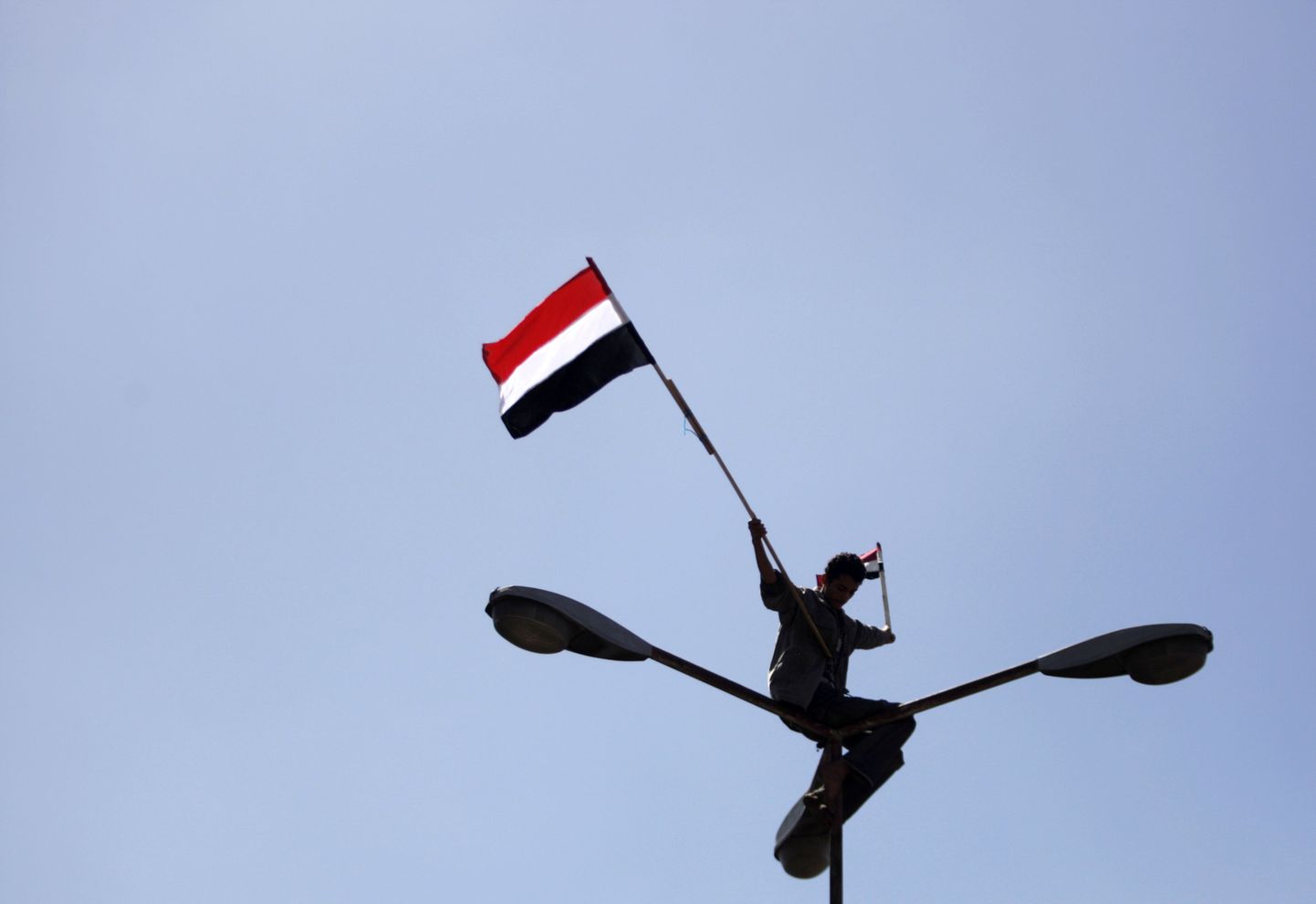 Jeemeni rahvuslippu lehvitav mees laternaposti otsas.