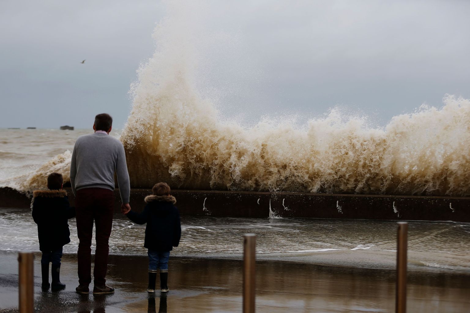 A man and children watch waves crashing against a tidal wall on January 4, 2018 in Asnelles, orthwestern France, after storm Eleanor swept into Europe.
Eleanor, the fourth winter storm to hit Europe since December, swept into the continent on January 3 after battering Britain and Ireland. / AFP PHOTO / CHARLY TRIBALLEAU
