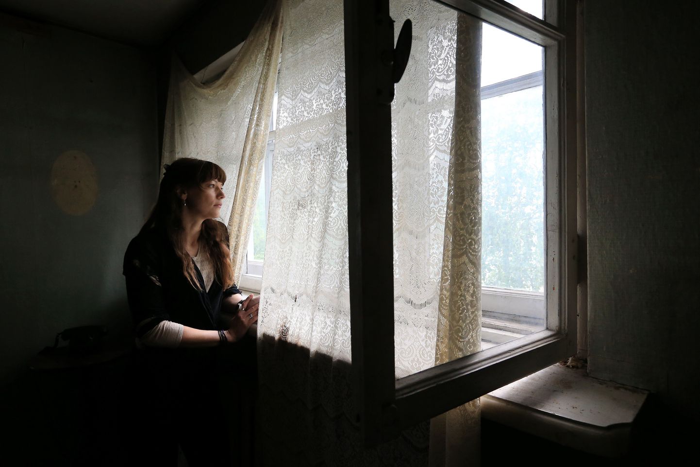 Evelin Salumaa vaatab välja aknast, mis võimaldas tal näitusele «Endspiel» liita puuvõrast ja kardinatest tekkiva valguse ja varjude mängu.