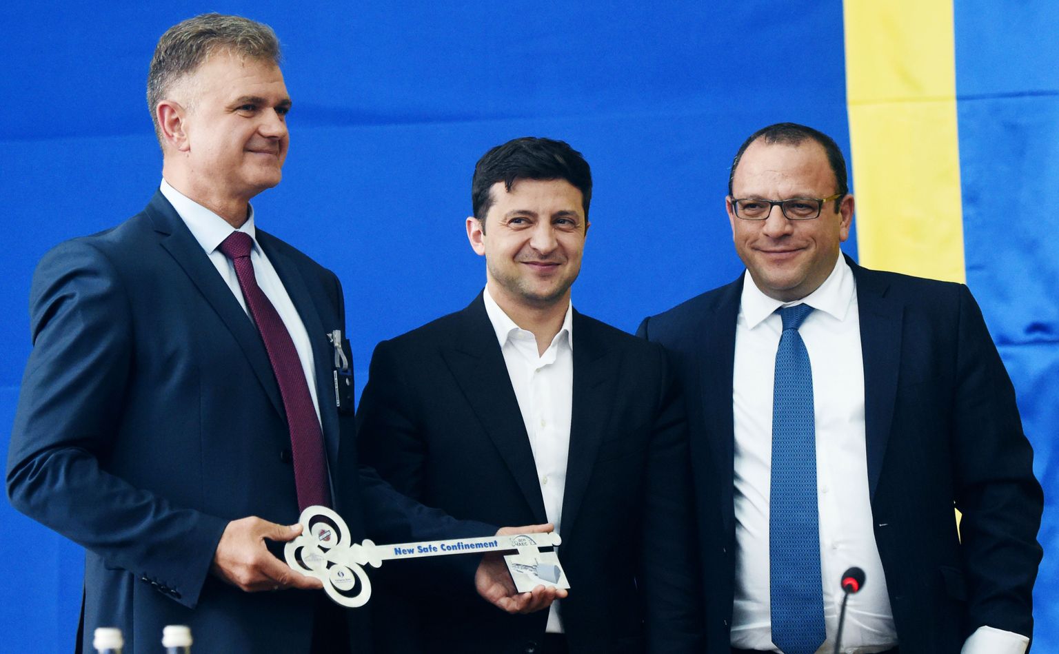 Černobiļas kodolspēkstacijas ģenerāldirektors Sergejs Kalašņiks, Ukrainas prezidents Volodimirs Zelenskis un Novarka Cirille pozē ar simbolisku atslēgu ceremonijā par godu jaunam metāla kupolam.