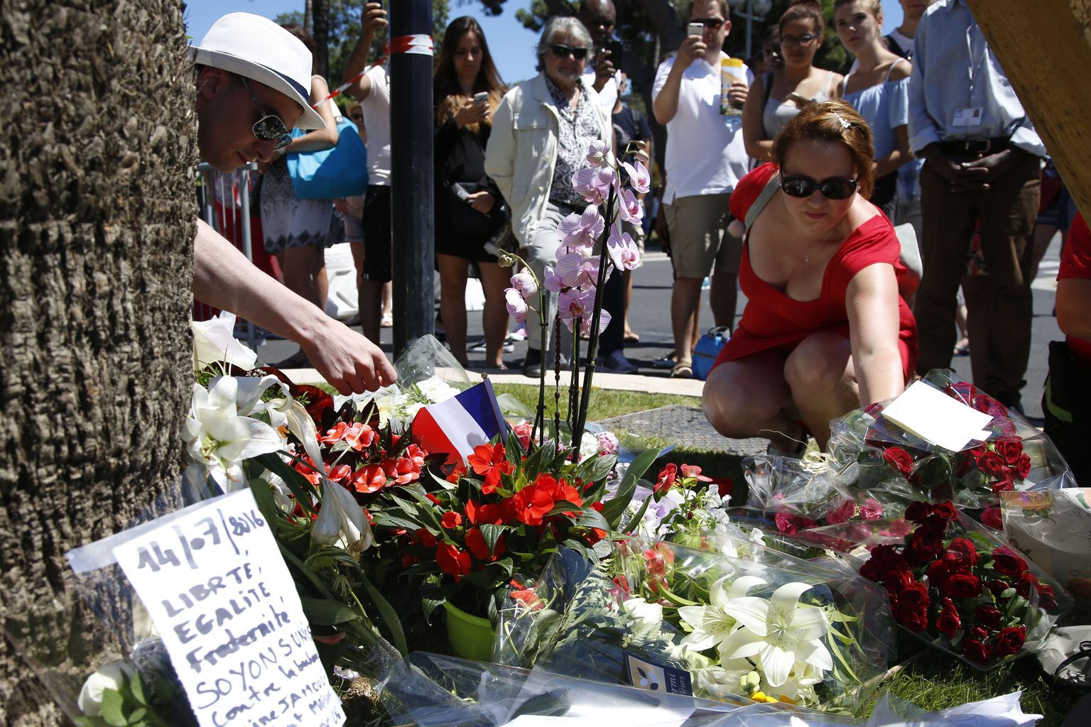 A woman places a bouquet of flowers as people pay tribute near the scene where a truck ran into a crowd at high speed killing scores and injuring more who were celebrating the Bastille Day national holiday, in Nice, France, July 15, 2016. REUTERS/Pascal Rossignol