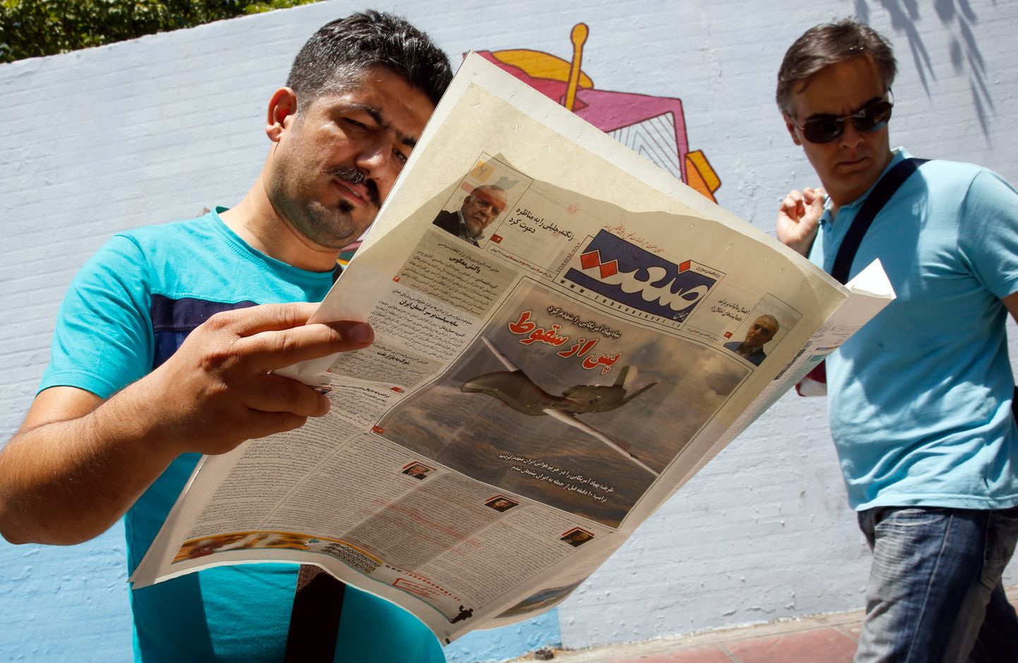 Iraani mees lugemas päevalehte Sanaat, kus kirjutatakse USA drooni allatulistamisest. Esilehel on pilt USA droonist ja pealkiri "Pärast allakukkumist".