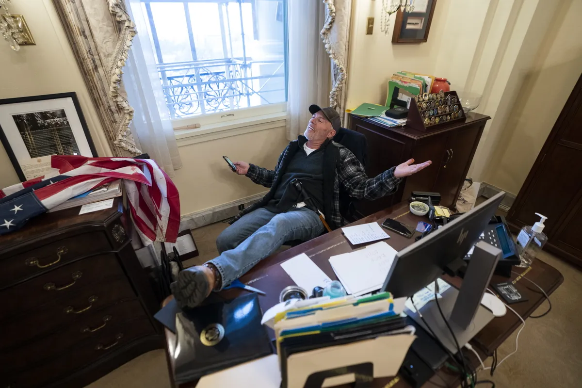 A supporter of US President Trump sits on the desk of US House Speaker Pelosi, after Trump supporters breached the US Capitol security in Washington, DC, USA, 6 January 2021.