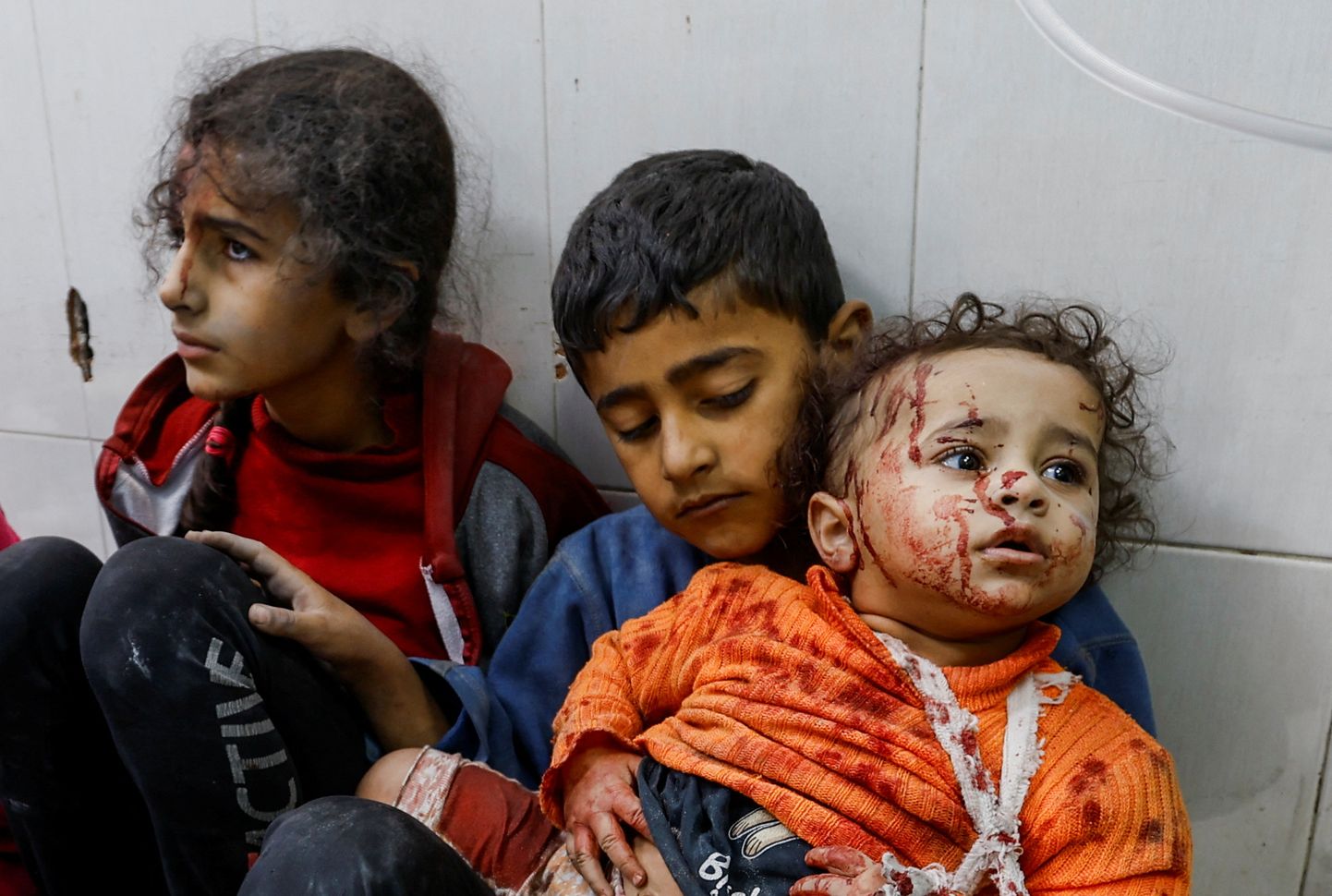 Раненые палестинские дети сидят на полу в больнице ​​после израильских ударов.