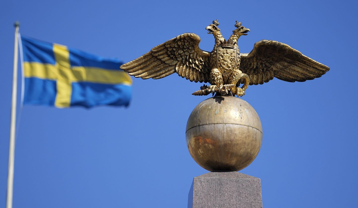 Российский двуглавый орел на фоне флага Швеции на Рыночной площади в Хельсинки.