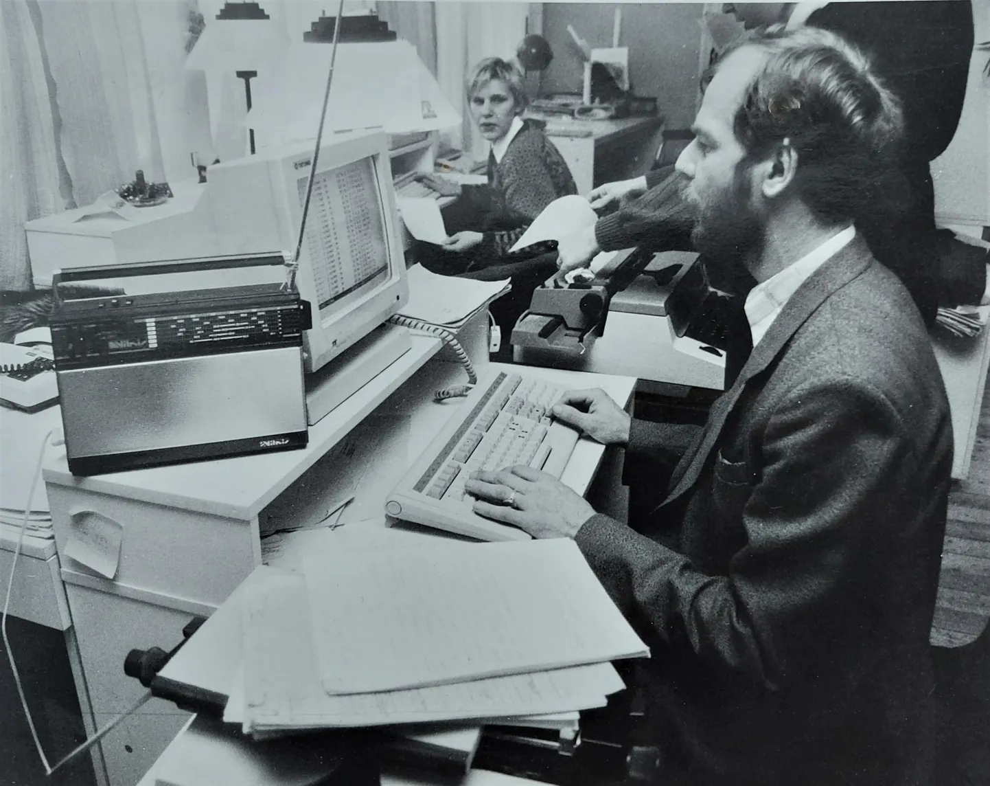 Postimehe toimetuses tõenäoliselt aastal 1991 tehtud fotol istuvad töölaua taga Vilja Kallaste (nüüd Kohler) ja Raimu Hanson, kes toksib toimetatud käsikirja arvutisse. Foto keskel on näha mehaanilist kirjutusmasinat.
