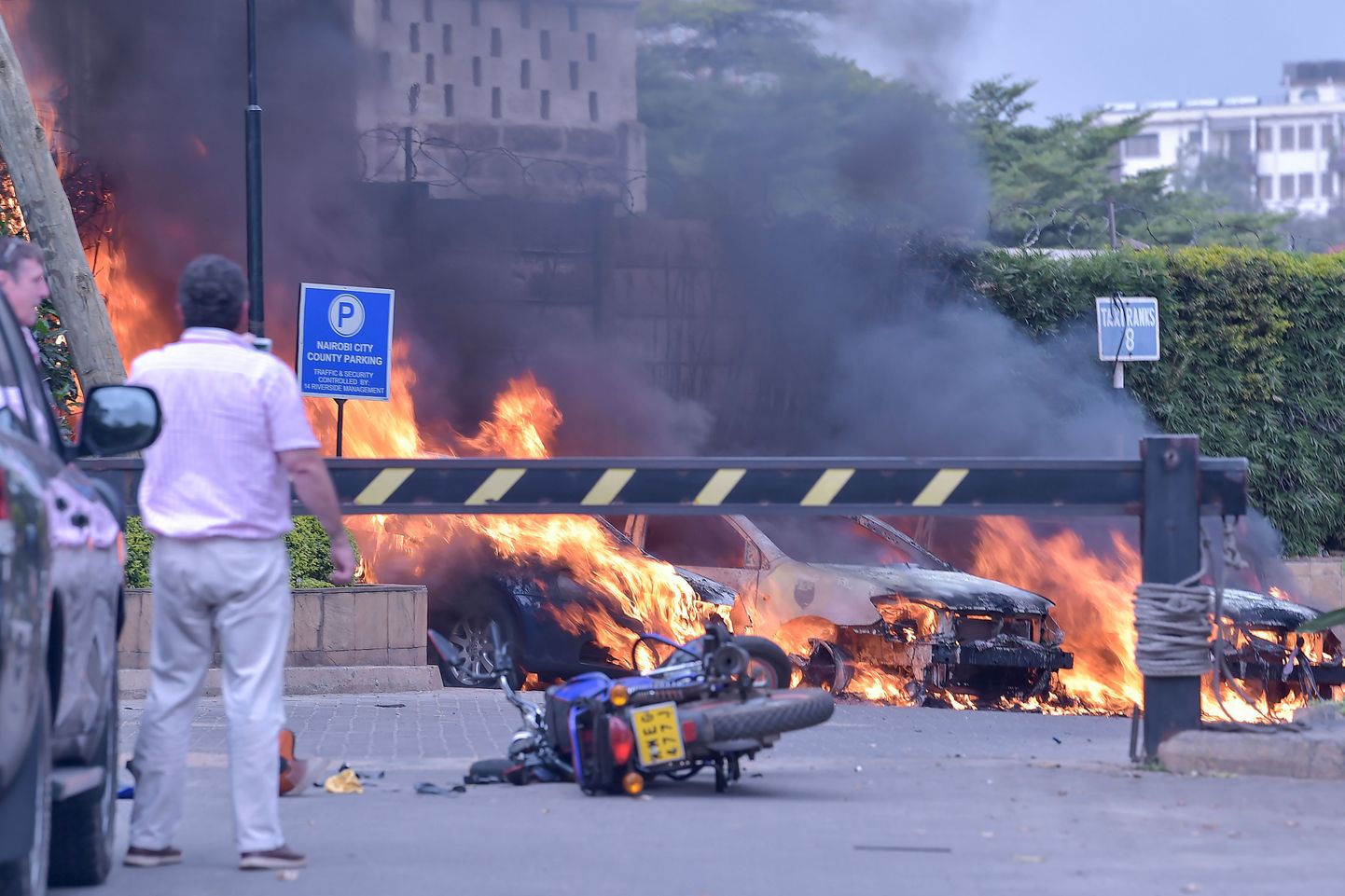 Kaks meest seisavad põlevate autode juures, mis on plahvatunud hotelli ees. Süü võtsid omaks Al-Shabaab islamistid. Pilt on artiklit illustreeriv.