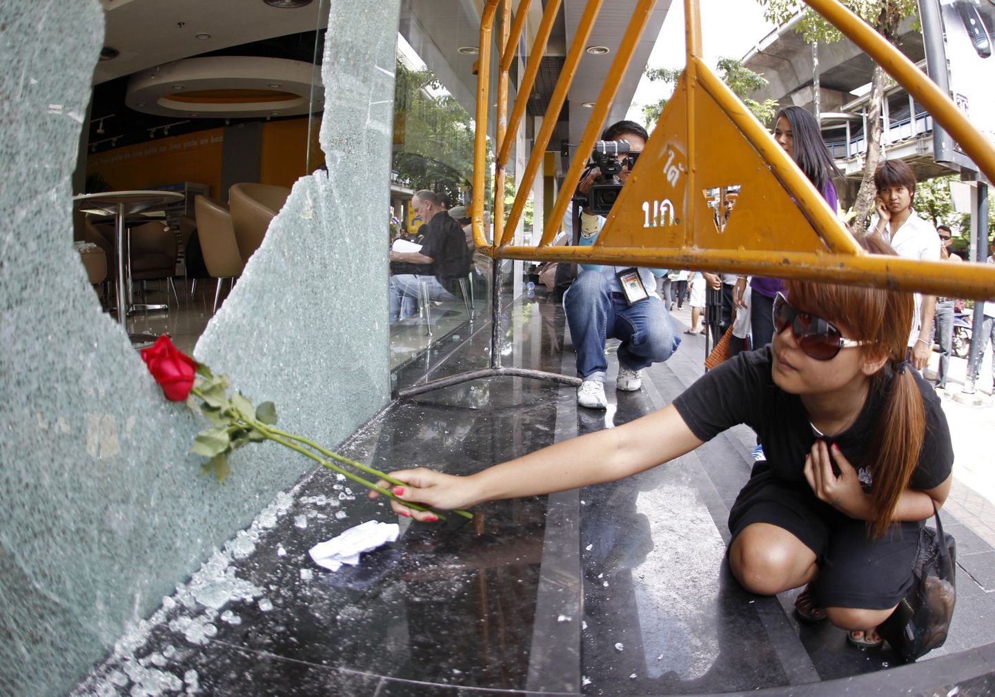 Naine asetab Bangkoki Silomi piirkonnas eilsete plahvatuste käigus purunenud kohvikuakna juurde punaseid roose.