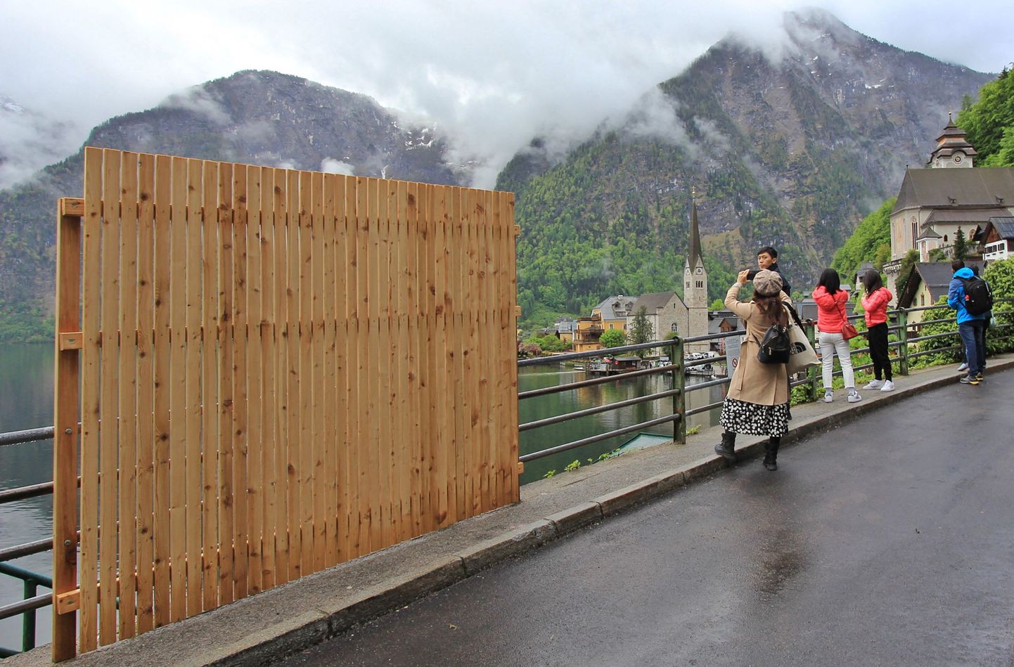 Временный деревянный забор частично загораживает живописный вид, пока посетители делают селфи на фоне пейзажа в туристическом городе Гальштат, Австрия, 15 мая 2023 года.