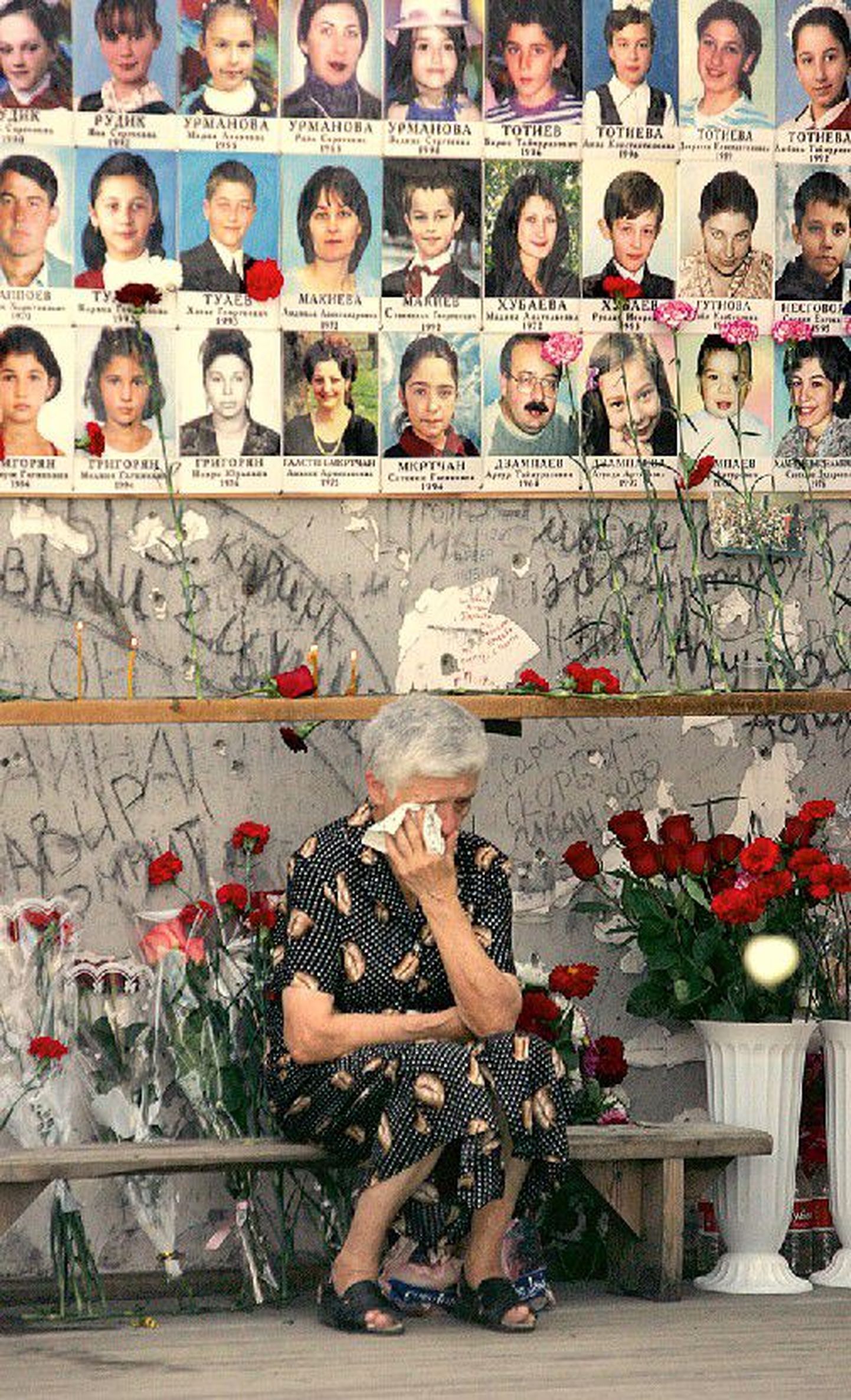 Пожилая женщина горько плачет на развалинах бесланской школы, вспоминая жертв трагических событий.
