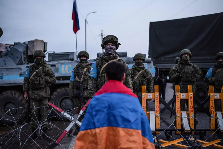 Протестующий с армянским национальным флагом стоит перед российскими миротворцами, блокирующими дорогу возле Степанакерта, столицы самопровозглашенного Нагорно-Карабахского региона Азербайджана, 24 декабря 2022 года.