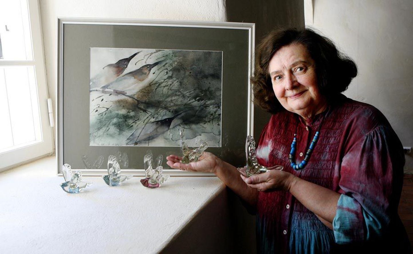 Maie-Ann Raun näituse ülespaneku ajal oma klaasist lindudega, kes praegu juba õhus lendavad. Taustal Ene Pika maal