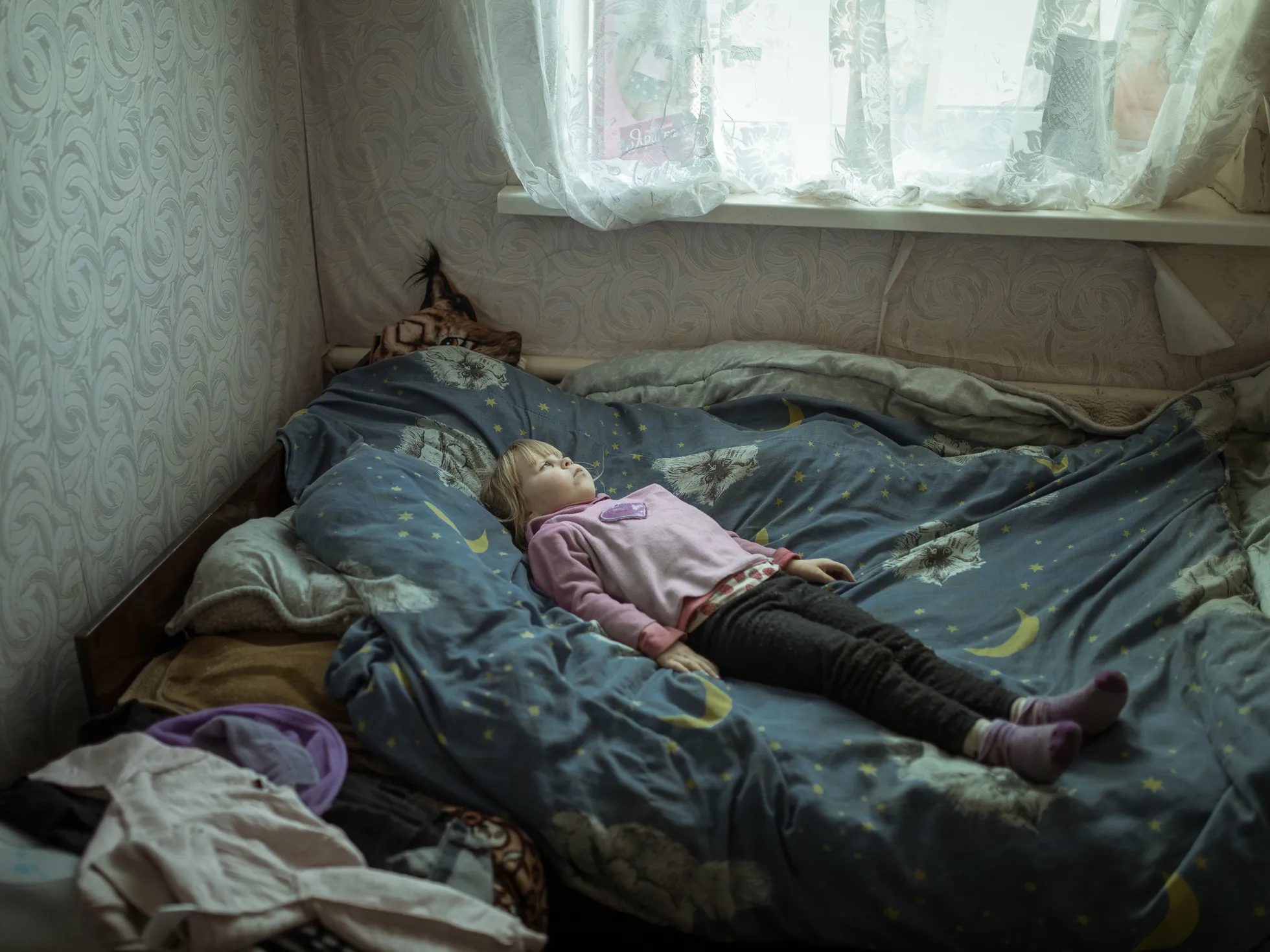 Kaevikute taga. Trauma läbi elanud ja paanikahoogude all kannatav Anhelina (6) pärast oma külast põgenemist, lebamas voodis oma uues kodus. Borštšivka, Ukraina. Euroopa, üksikfotod.