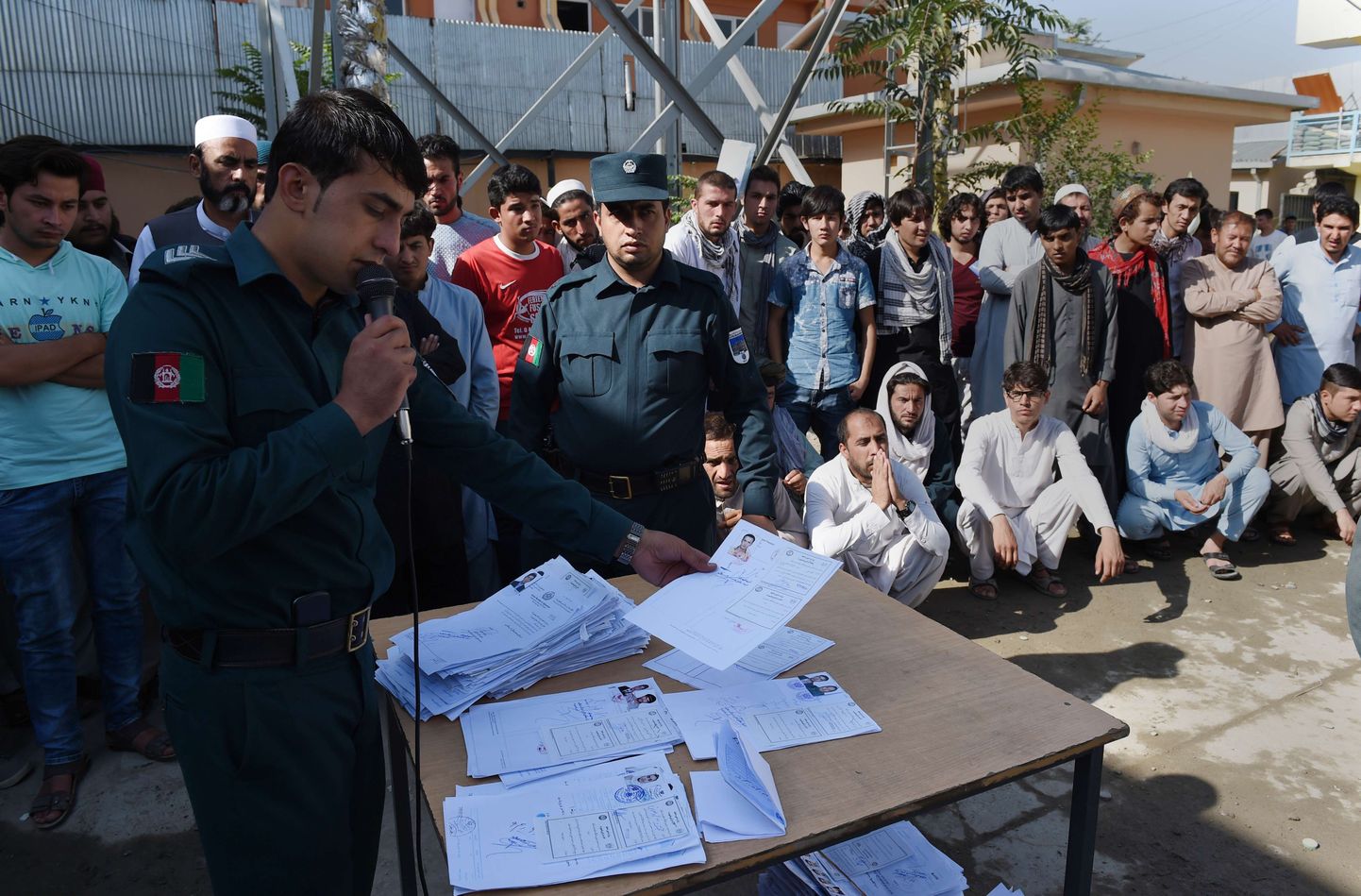 Afganistani politseinik hõigub mikrofoni kaudu passitaotlejate nimesid passijaoskonna õuel Kabulis.
