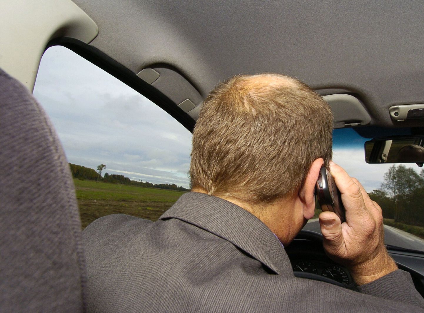 Мужчина разговаривает по мобильному телефону за рулем.