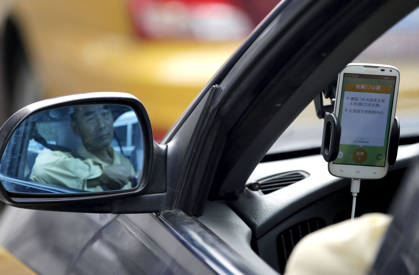 A taxi driver is reflected in a side mirror as he uses the Didi Chuxing car-hailing application in Beijing, China, September 22, 2015. REUTERS/Jason Lee/File Photo