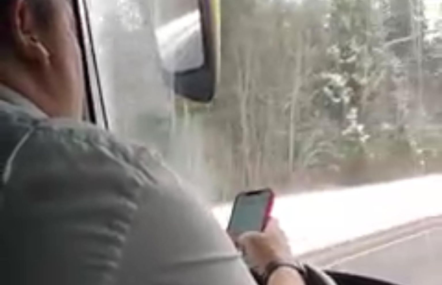 Водитель автобуса смотрит в телефон во время вождения.