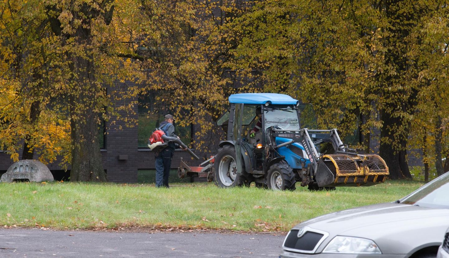 Tartu kesklinnas puhastab tööline lehepuhuriga lehtedest traktorit.