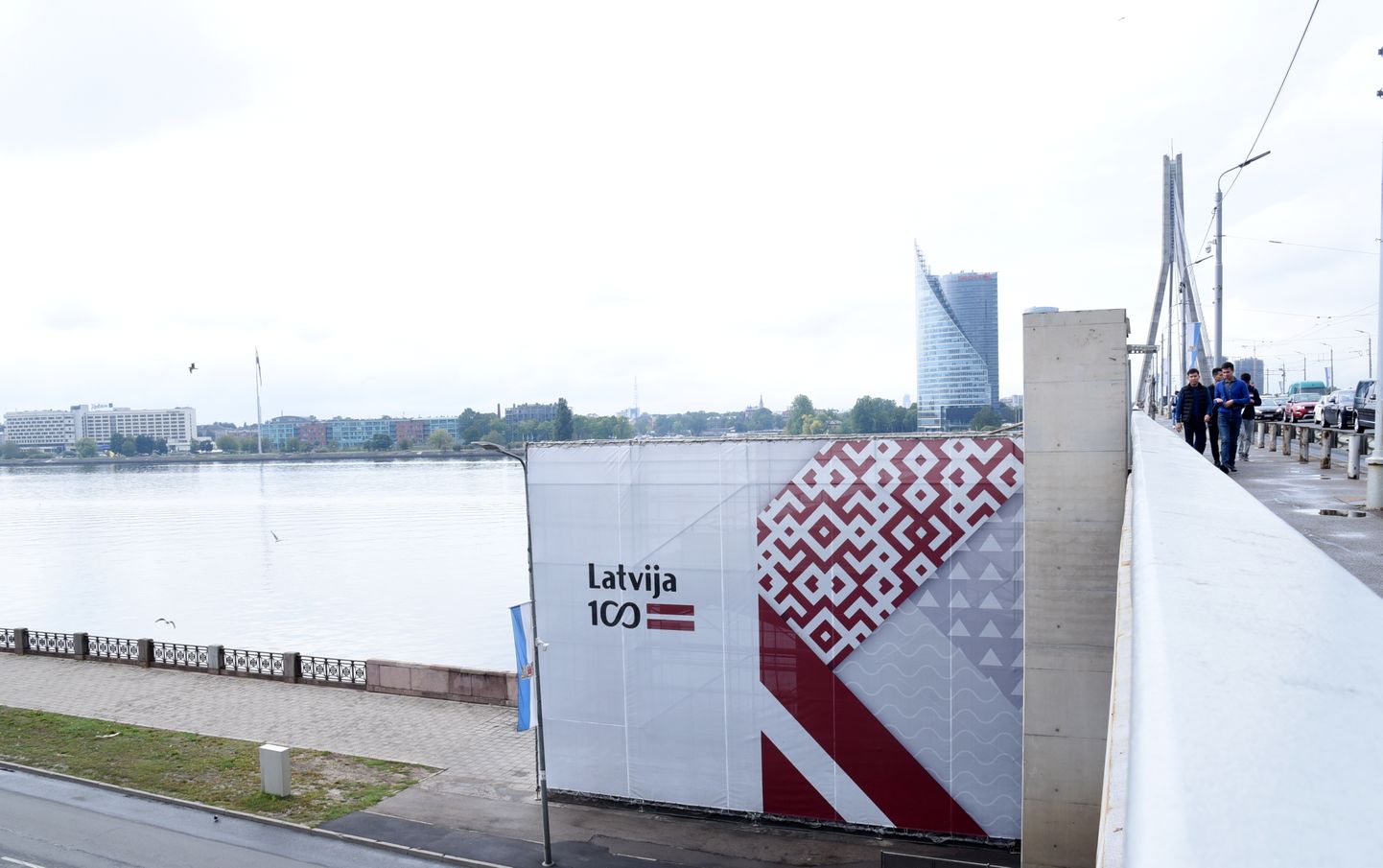 Ar aizsegu, kurā redzama Latvijas valsts simtgades simbolika, piesegtās sliktajā stāvoklī esošās Vanšu tilta kāpnes Daugavas labajā pusē.