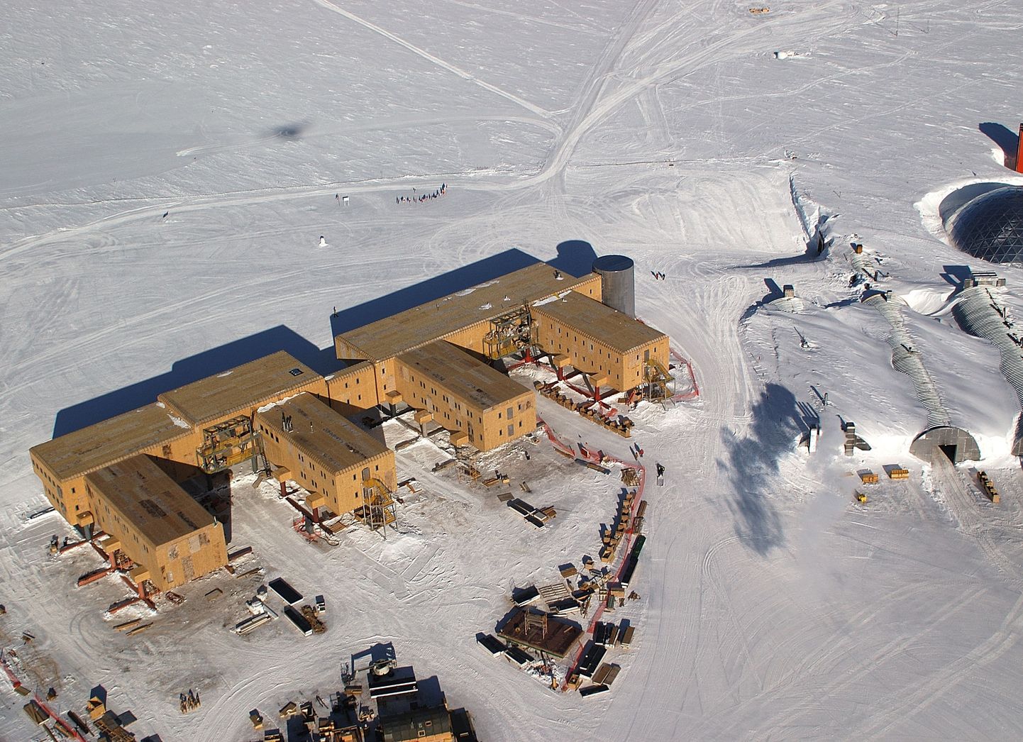 Amundsen-Scotti polaarjaam lõunapoolusel. Pildil enamvähem keskel on hoone taga enne teerada näha ka lippudega varustatud tseremoniaalne poolus ja geograafilise pooluse tähis.