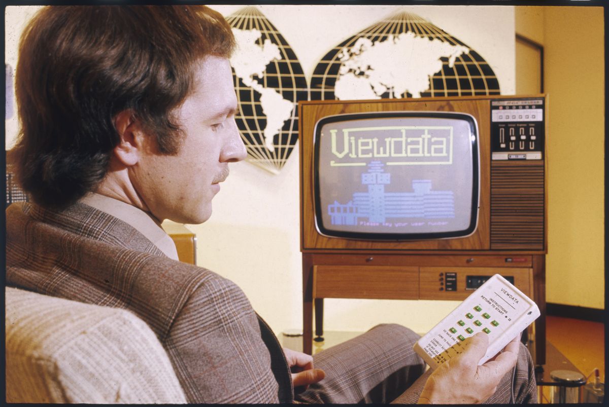 A fashionable young man in a  beige jacket adjusts the text service on his television with  the aid of the latest gadget  - a remote control!      Date: 1970s