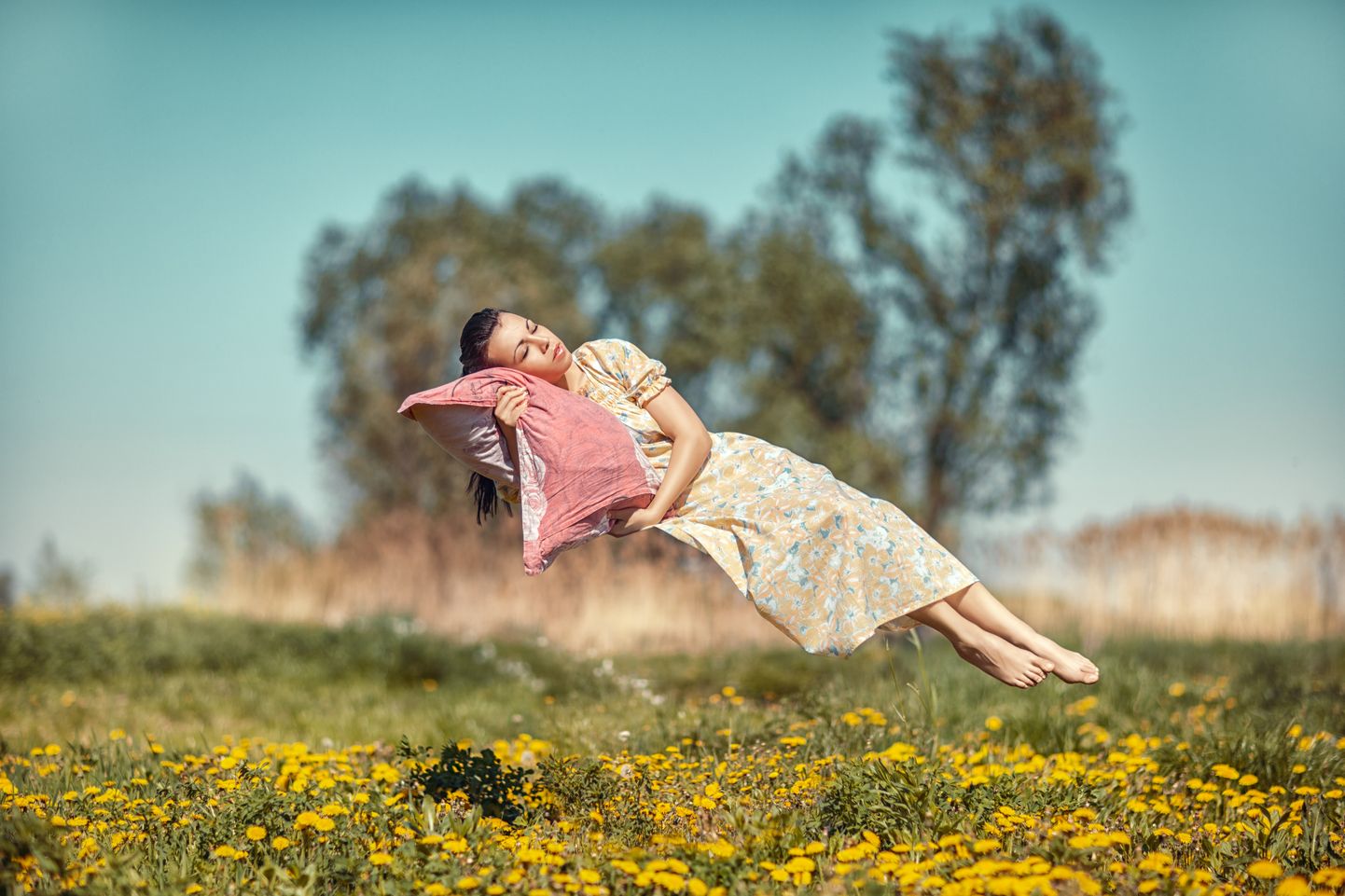 Girl hovers and sleeps on a pillow over a beautiful meadow.