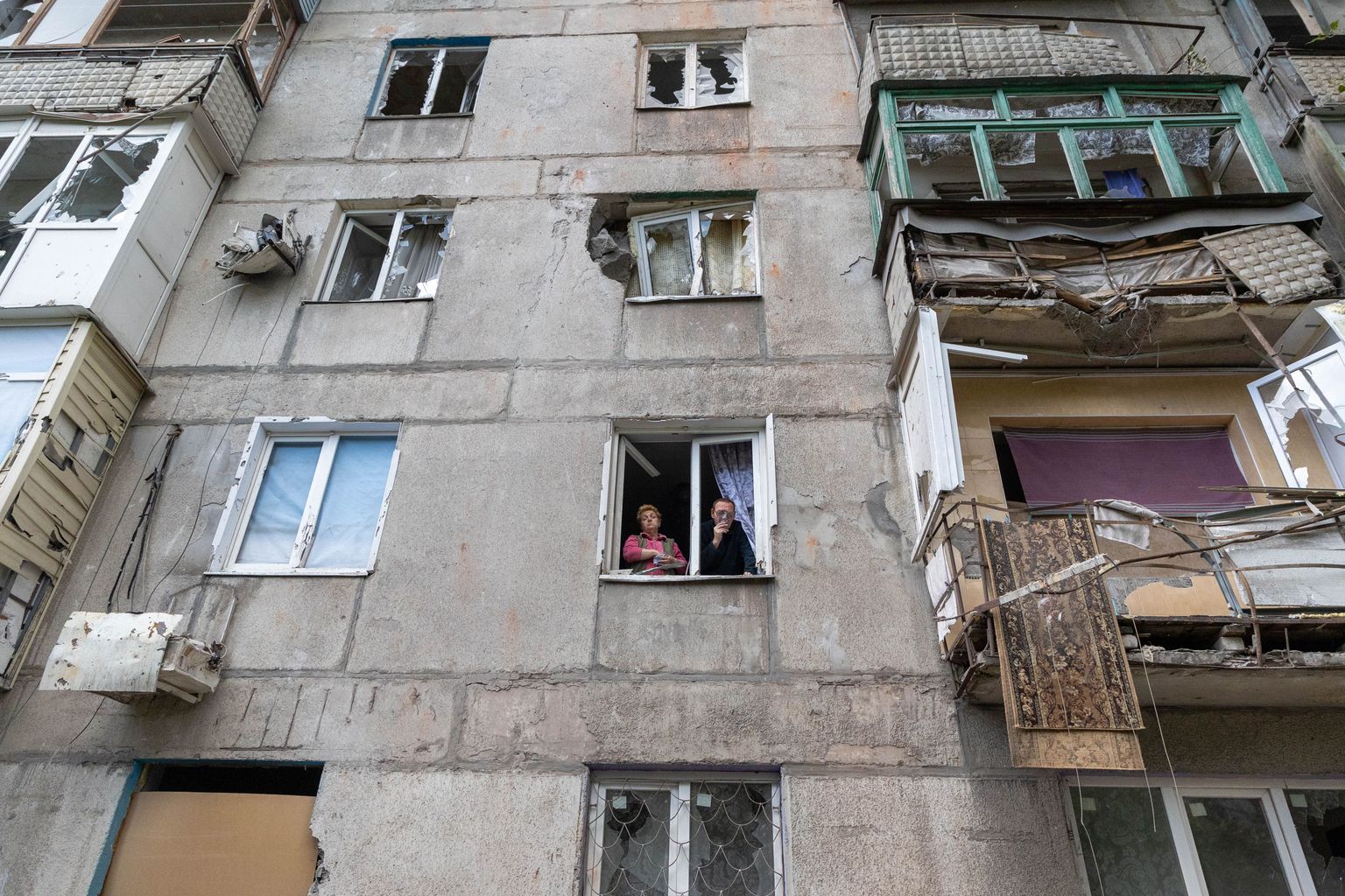 Наталья и Александр, жители Торецка, города в Донецкой области, выглядывают из окна своей разрушенной квартиры.
