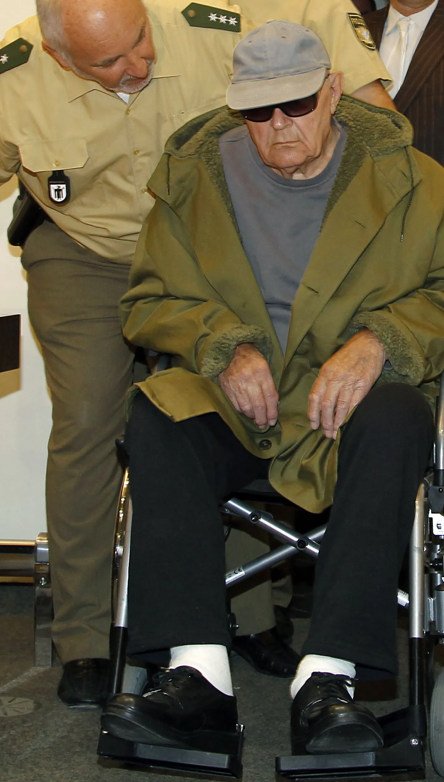91-aastane John Demjanjuk (ratastoolis) koos politseinikuga.