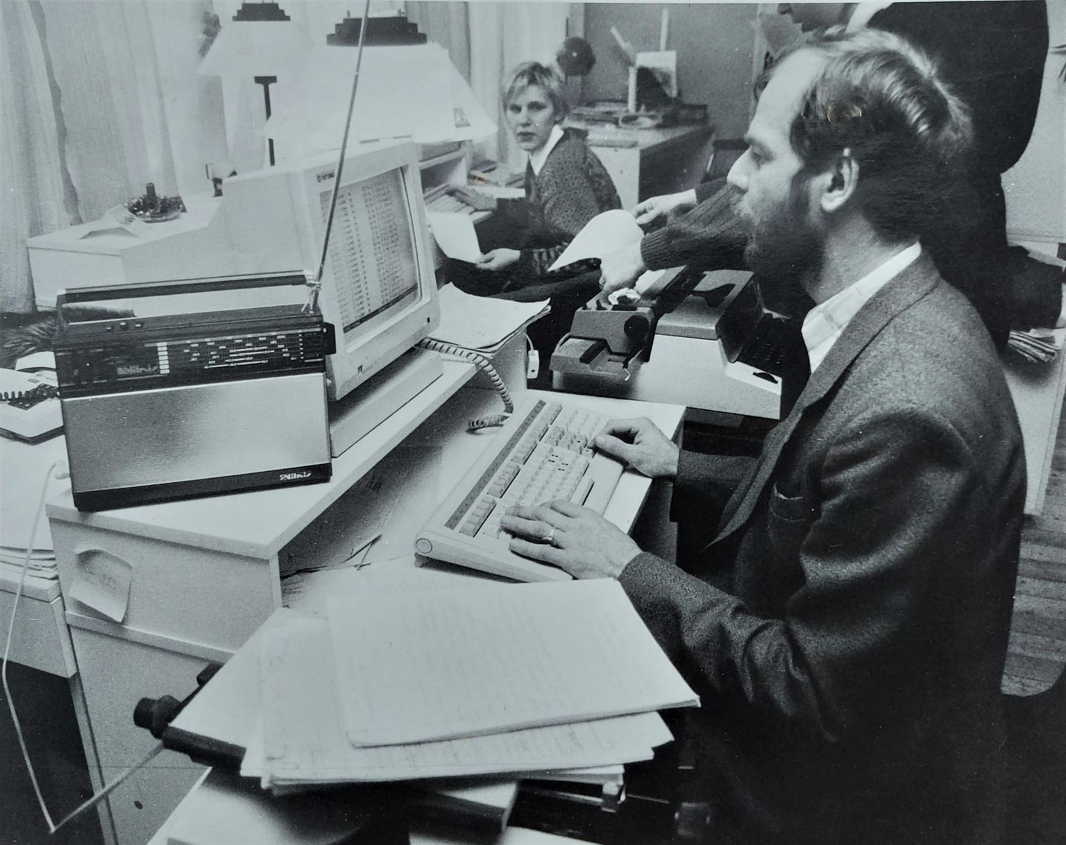 Postimehe toimetuses tõenäoliselt aastal 1991 tehtud fotol istuvad töölaua taga Vilja Kallaste (nüüd Kohler) ja Raimu Hanson, kes toksib toimetatud käsikirja arvutisse. Foto keskel on näha mehaanilist kirjutusmasinat.