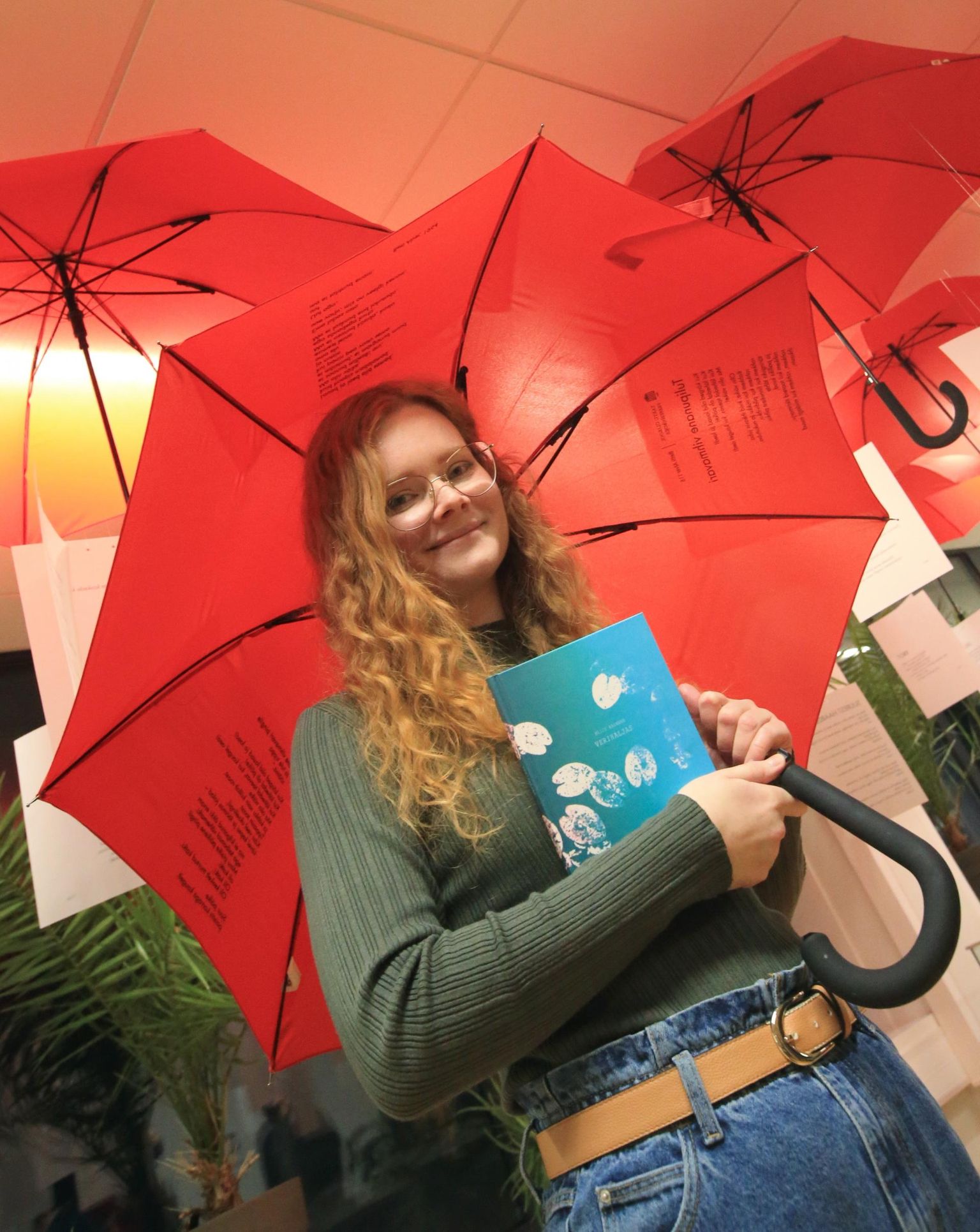 Aliis Aalmann hoiab käes auhinna toonud luulekogu, pea kohal Betti Alveri loomingu näituse kujunduses kasutatud vihmavarjud.