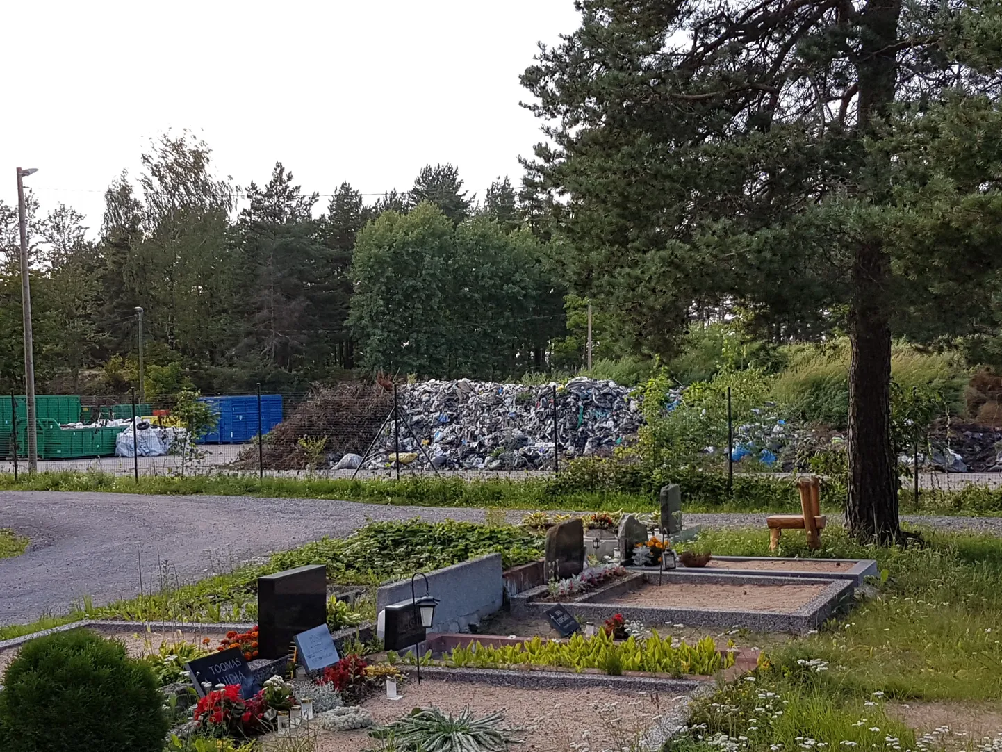 От могил станцию по приему отходов отделяет всего несколько метров и тонкая металлическая сетка. За ней – контейнеры, использованные покрышки и огромная, уже поросшая травой куча, состоящая из веток, досок и мусорных пакетов.