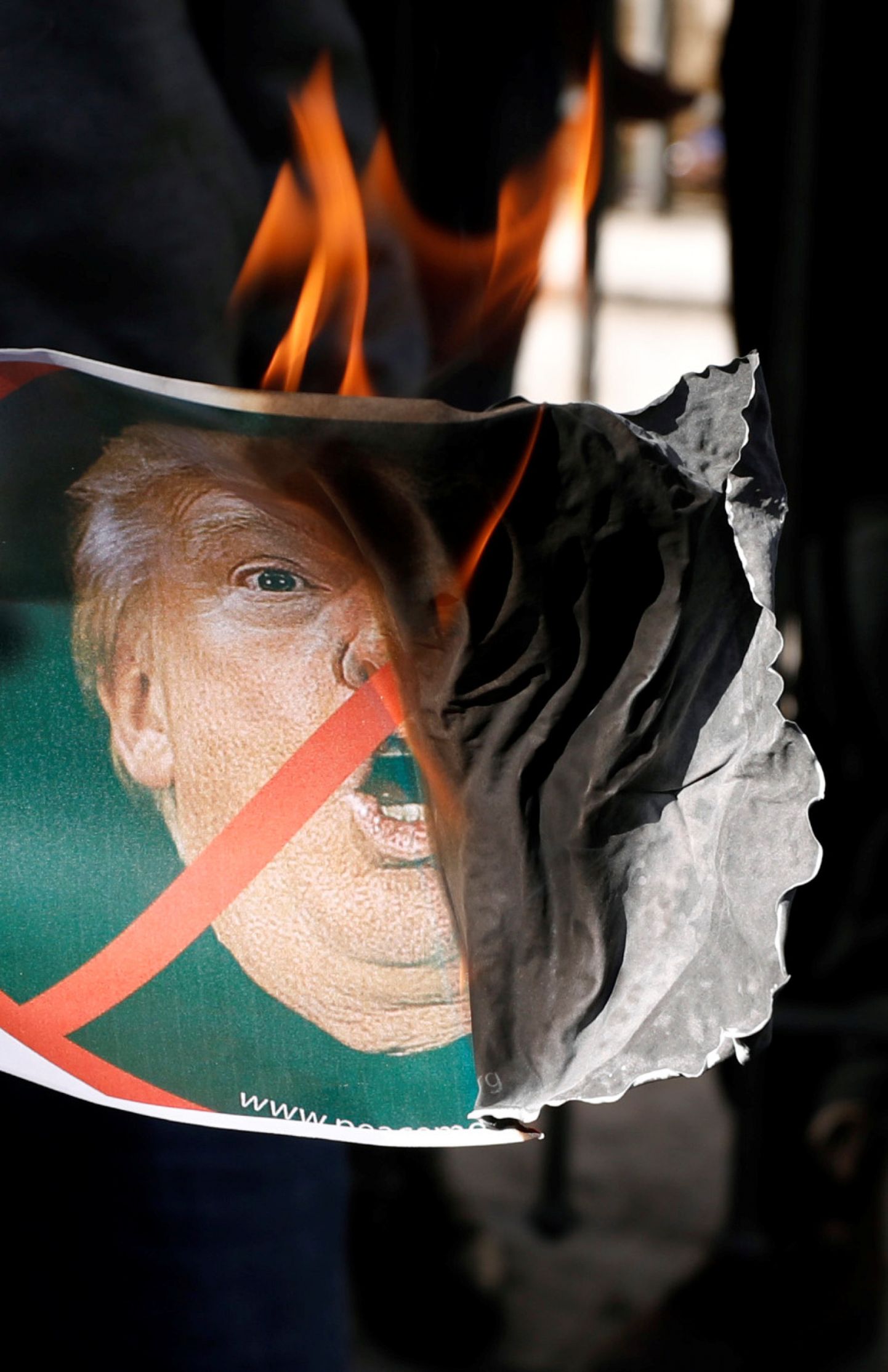 Протестующий сжигает плакат с портретом Дональда Трампа.