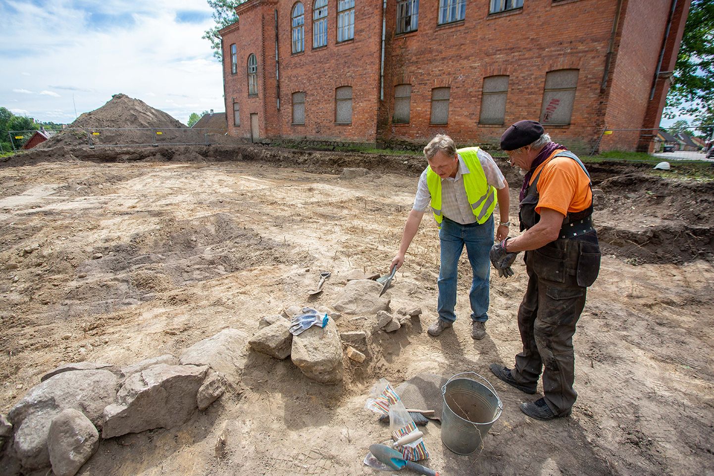 Arheoloog Peeter Piirits (vasakul) ja kaevetöid tegev Jaak Salmar näitavad vundamenti, mis tuli maapõuest välja.