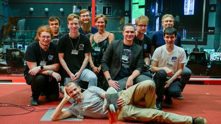 ESTCube-2 tiim mõne päeva eest Kourou kosmosekeskuses enne seda, kui start edasi lükati. Ees lamab Tartu observatooriumi direktor Antti Tamm. Tema taga (vasakult paremale) tarkvarainsener Kirill Anohin, elektroonikainsener Karl Mattias Moor, mehaanikainsener Sergei Kuzmin, süsteemiinsener Janis Dalbinš, elektroonikainsener Michelle Lukken, projektijuht Hans Teras, tarkvarainsener Laur Edvard Lindmaa, tagapool missioonijuhtimise arendaja Kevin Wirth, eespool juhtiv süsteemiinsener Kristo Allaje.