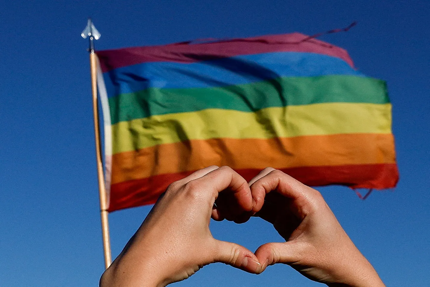 Inimene hoidmas oma käsi südamekujuliselt LGBT vikerkaarelipu ees.
