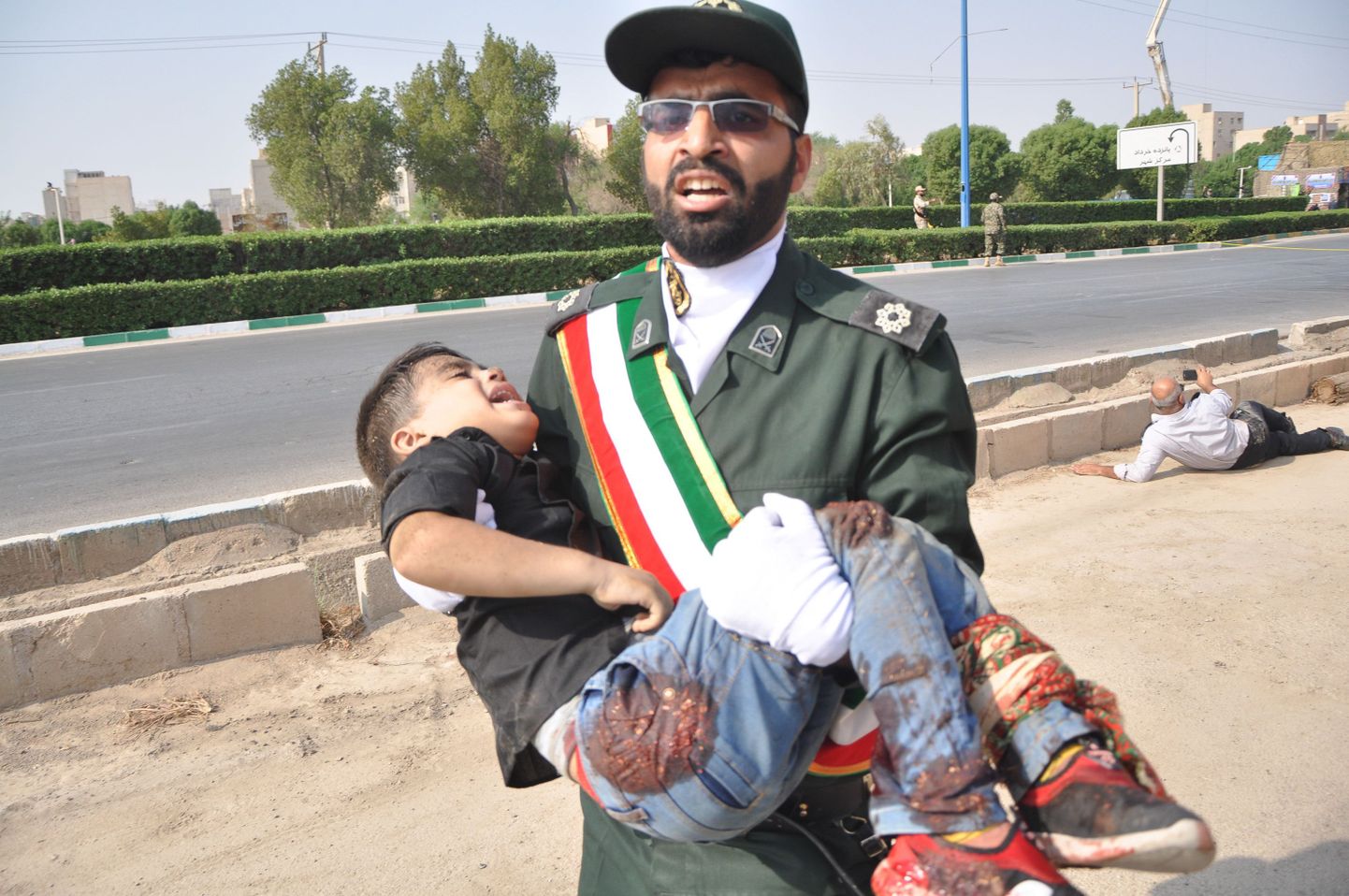 Военнослужащий Корпуса стражей исламской революции уносит раненого ребенка с места стрельбы.