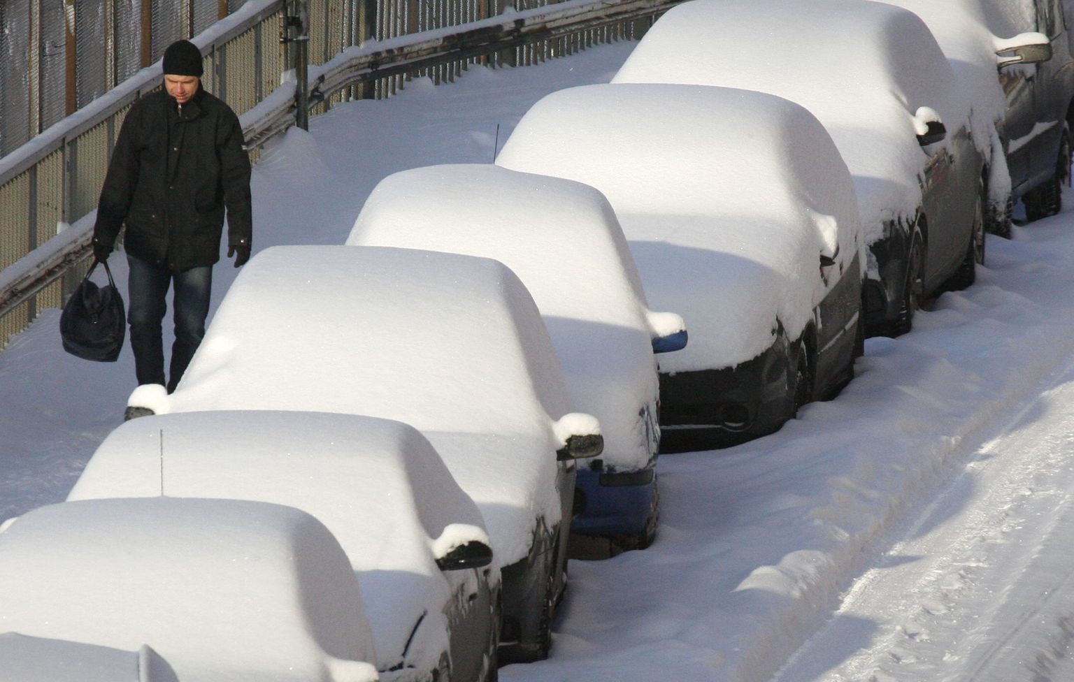 Jalakäija möödub lume alla maetud autodest Stockholmis.