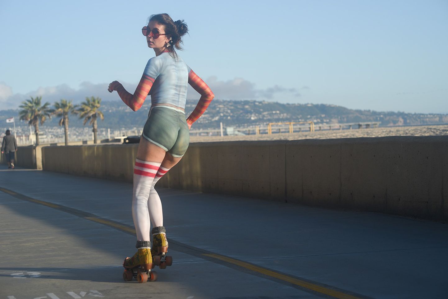 Обнаженная девушка катается на роликах по набережной в солнечной Калифорнии. Ее тело разрисовано боди-артом.