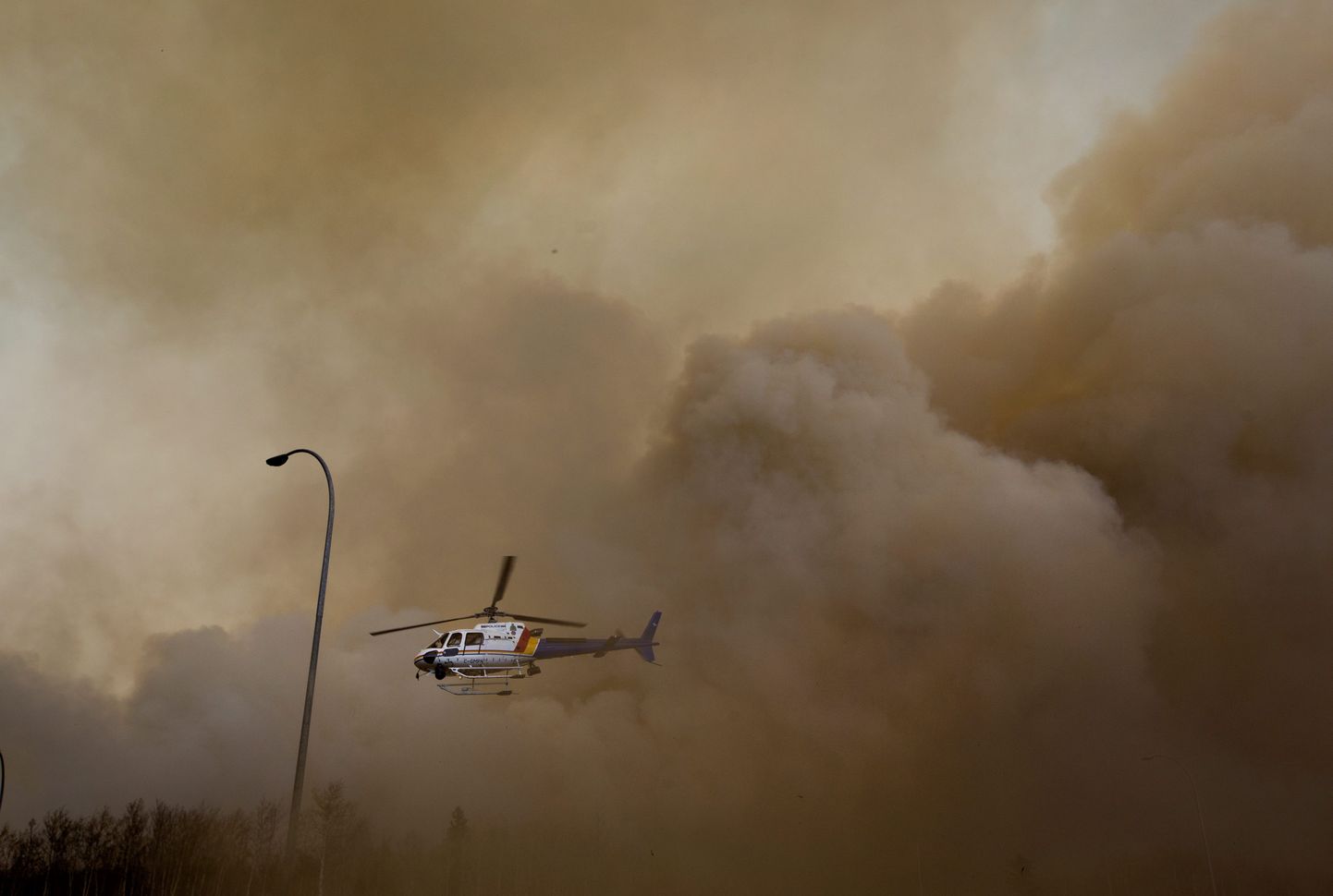 A police helicopter lifts off through dust and smoke near a wildfire in Fort McMurray, Alberta, Friday, May 6, 2016. Officials said shifting winds were giving the embattled northern Alberta city a break, but they added the fire that forced 80,000 people from their homes remained out of control and was likely to burn for weeks. (Jason Franson/The Canadian Press via AP)