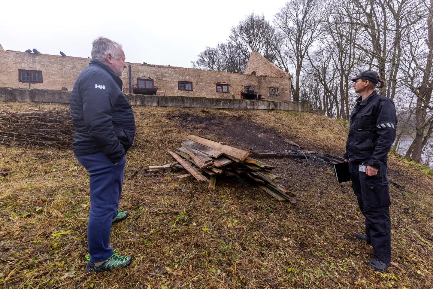 Porkuni külavanem Eigo Laur (vasakul) ja päästeameti menetleja Tanel Sepajõe põlenud tallihoone ees. Meeste vahel on ehitusprahi põletamise koht, kust õnnetus alguse sai.