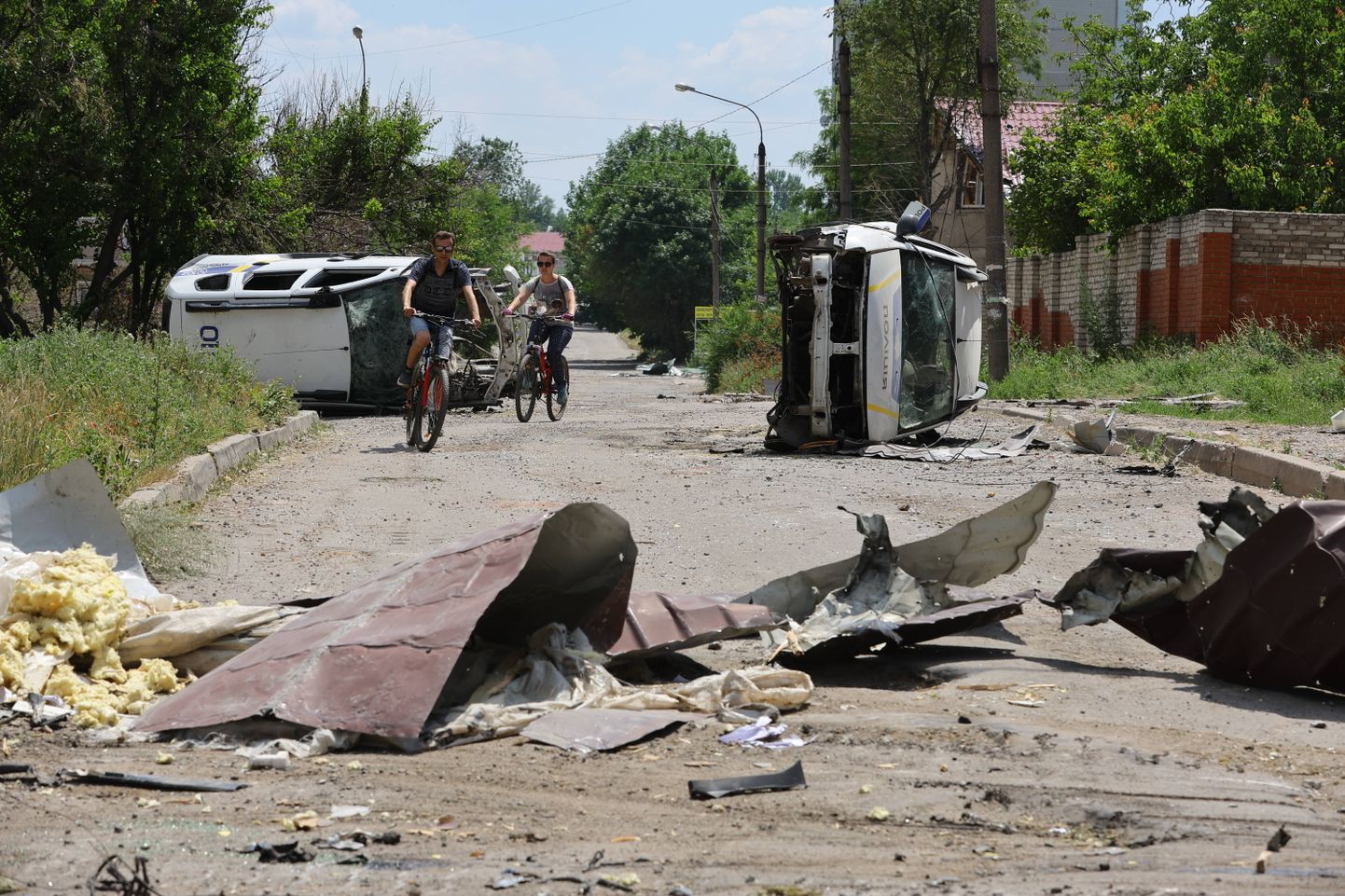 Жители на велосипедах проезжают мимо разбитой полицейской машины в Лисичанске (Луганская область), 4 июля 2022 года.