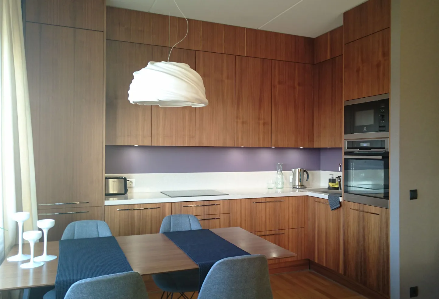 Дизайн современной кухни тяготеет к простоте. Как правило, это прямые лаконичные формы с минимумом фурнитуры на фасадах. Верхние шкафы до потолка позволяют максимально использовать пространство, а также придают кухне законченный вид.