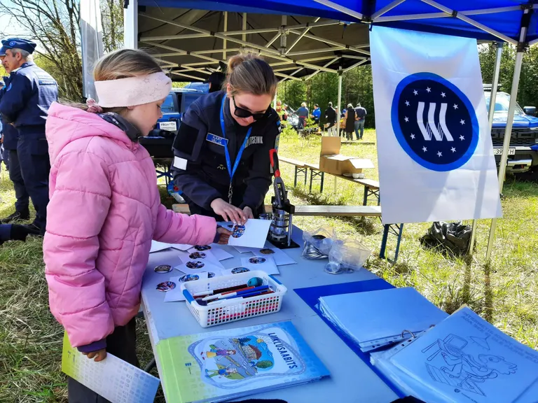 Laste liikluskasvatus käib tegevuse kaudu. Pildil sellekohase märgi vormimine politseiniku abiga.