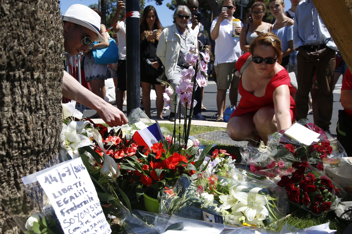 A woman places a bouquet of flowers as people pay tribute near the scene where a truck ran into a crowd at high speed killing scores and injuring more who were celebrating the Bastille Day national holiday, in Nice, France, July 15, 2016.   REUTERS/Pascal Rossignol