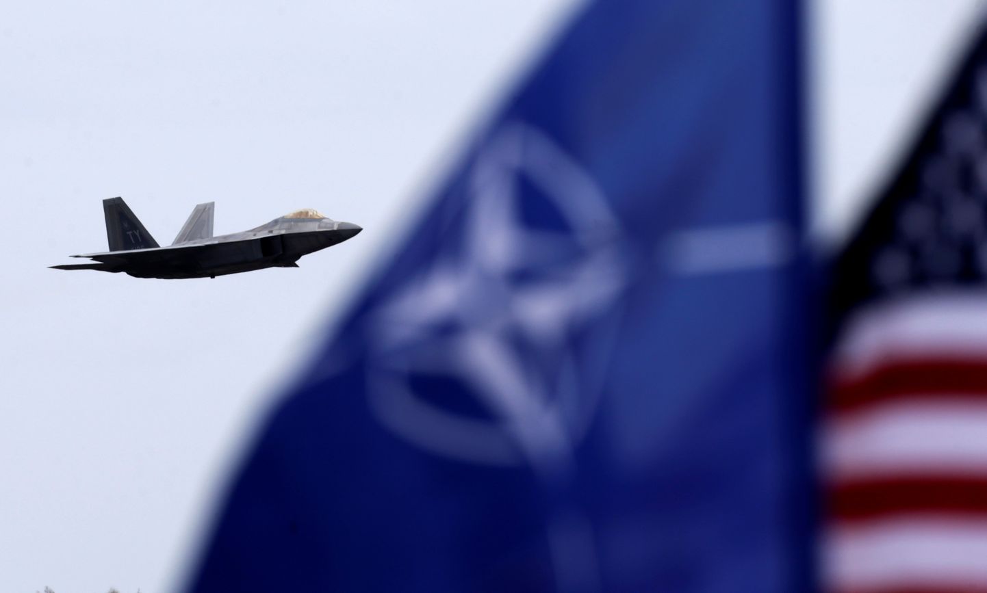 NATO ja USA lipud lehvivad, kui USA õhuväe hävitaja F-22 Raptor üle Leedus asuva Šiauliai õhuväebaasi lendab.