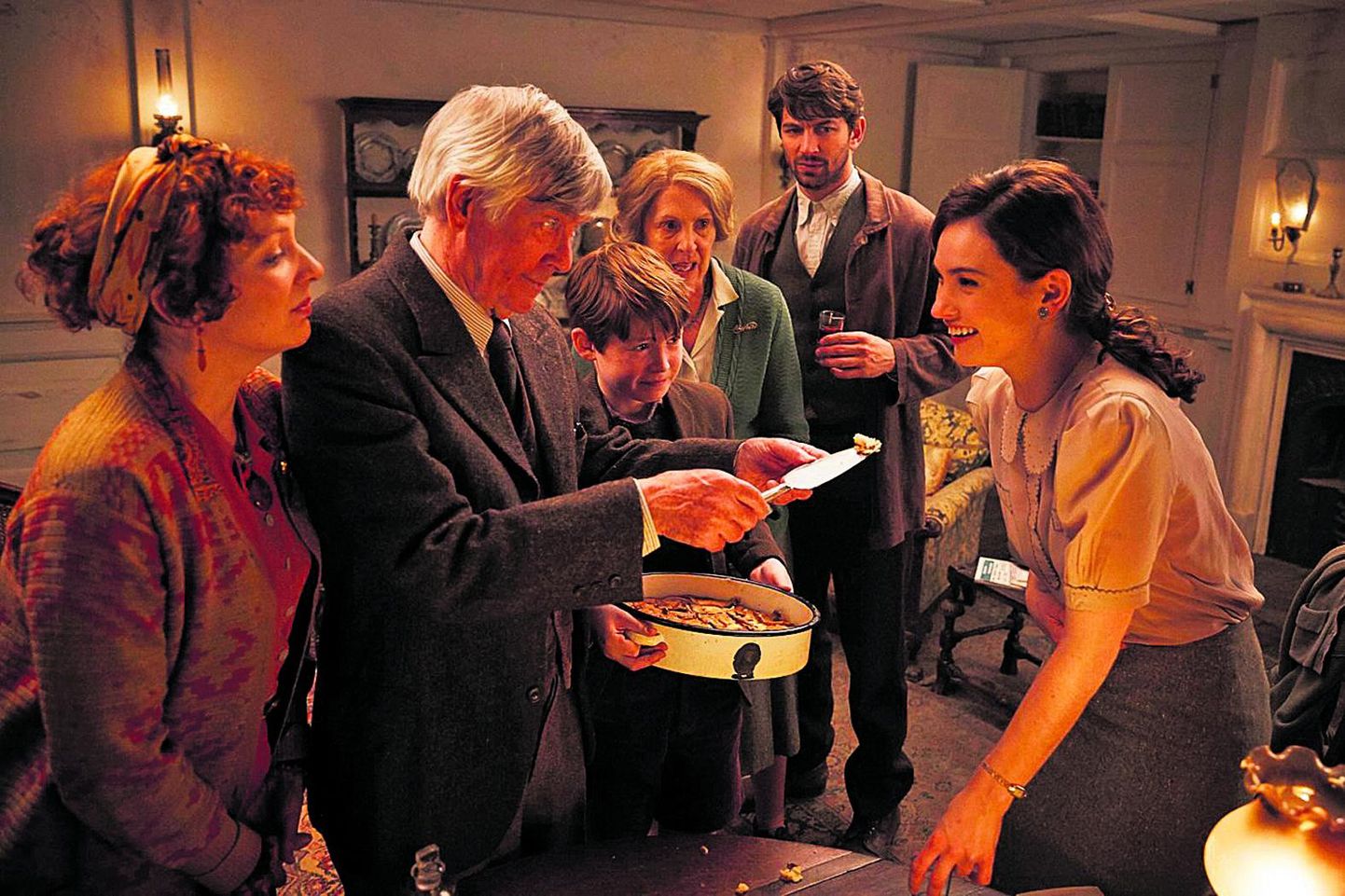 Kaader filmist «Guernsey kirjandus- ja kartulikoorepiruka selts” - paremal peategelane Juliet Ashton (Lily James), kes proovib kartulikoorepirukat.