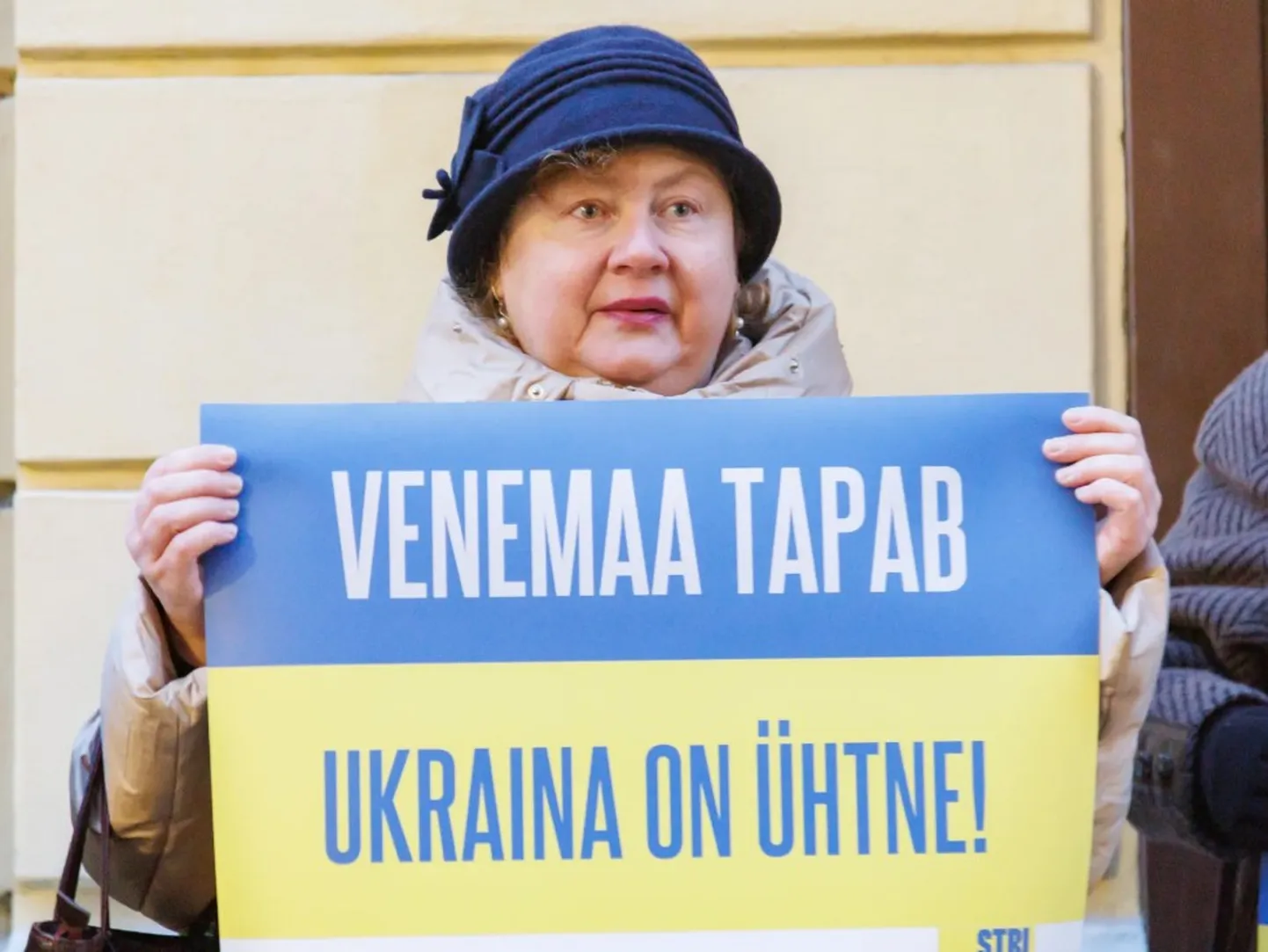 Плакат «Россия убивает. Украина едина» в руках участницы митинга в поддержку Украины, посольство РФ на улице Пикк, Таллинн, 22 января 2025 года.