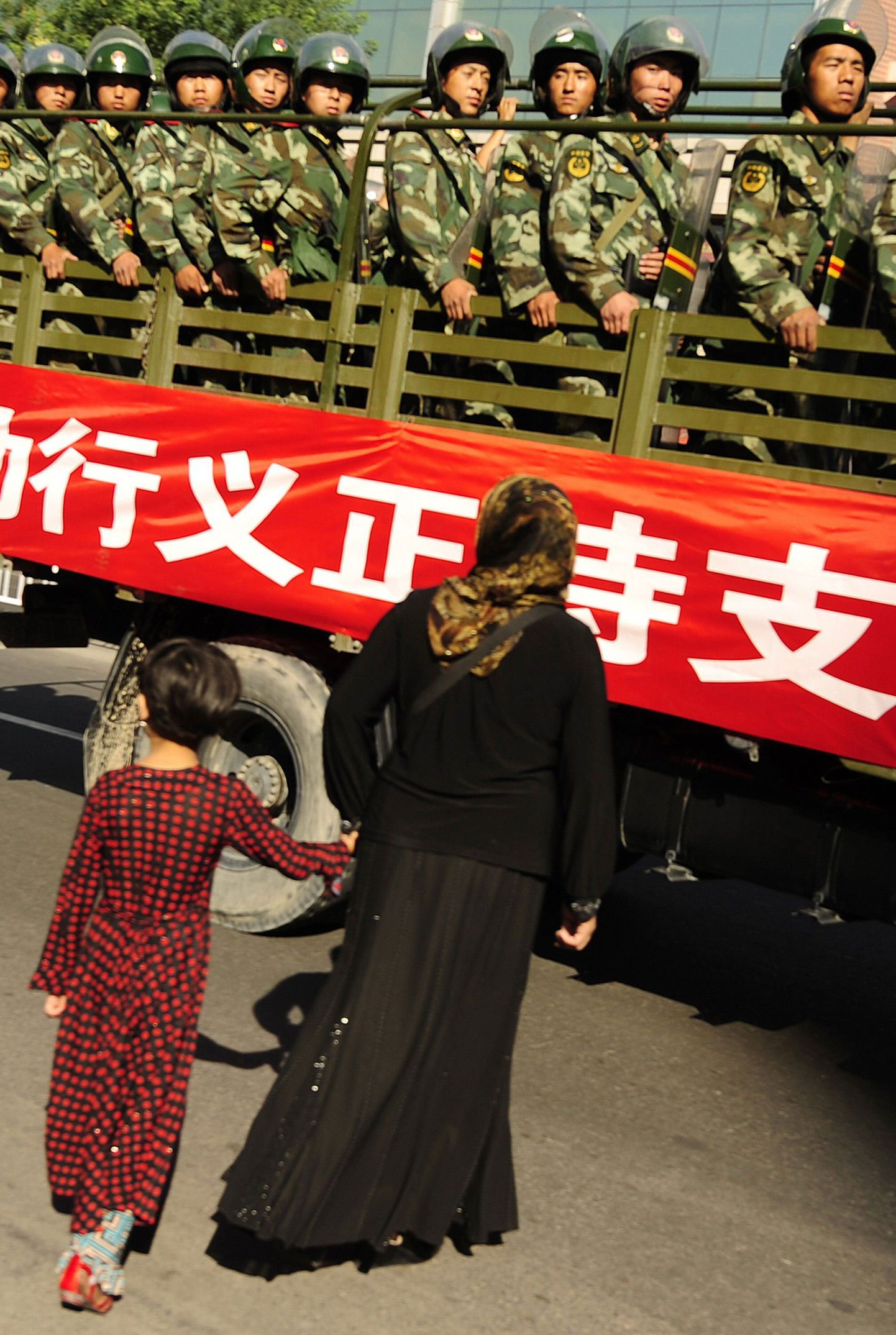 Uiguuri naine tütrega Hiina sõjaväeveoki taustal.